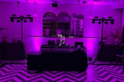 Salle décorée avec éclairage violet, table de mixage DJ au centre, enceintes et projecteurs sur trépieds.