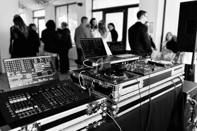 Équipement de DJ avec platines et ordinateurs dans une salle animée par des invités en arrière-plan.