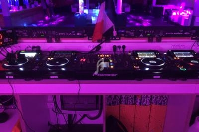 Poste de DJ avec plusieurs platines et une table de mixage, éclairé par une lumière violette dans un environnement de club.