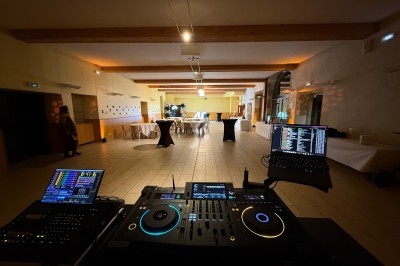 Vue d'une salle de réception vide avec une table de mixage et des équipements DJ au premier plan.