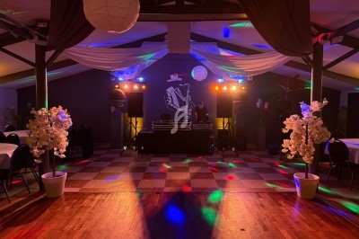 Salle de réception décorée avec des lumières colorées, une piste de danse et un DJ en arrière-plan.