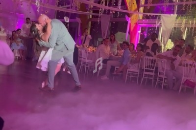Un couple danse au centre d'une salle décorée avec des lumières roses et des guirlandes suspendues, entouré d'invités assis.