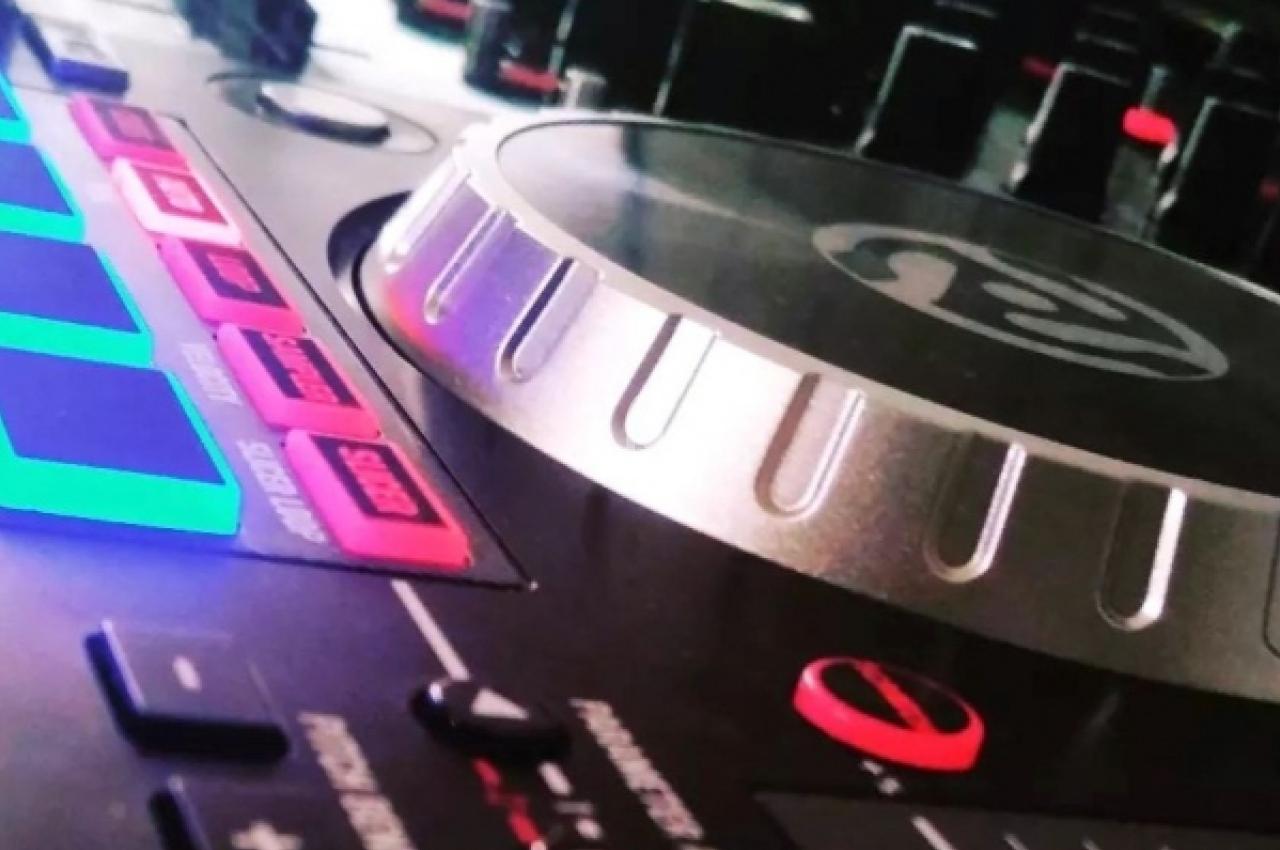 Table de mixage avec des boutons lumineux et un plateau rotatif argenté, utilisée pour la musique ou le DJing.