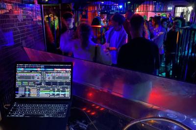 Table de mixage éclairée avec des lumières colorées, un ordinateur affichant un logiciel de DJ en arrière-plan.