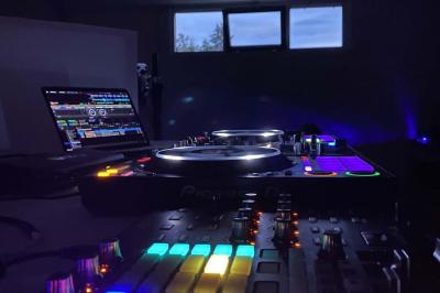 Table de mixage éclairée avec des lumières colorées, un ordinateur affichant un logiciel de DJ en arrière-plan.