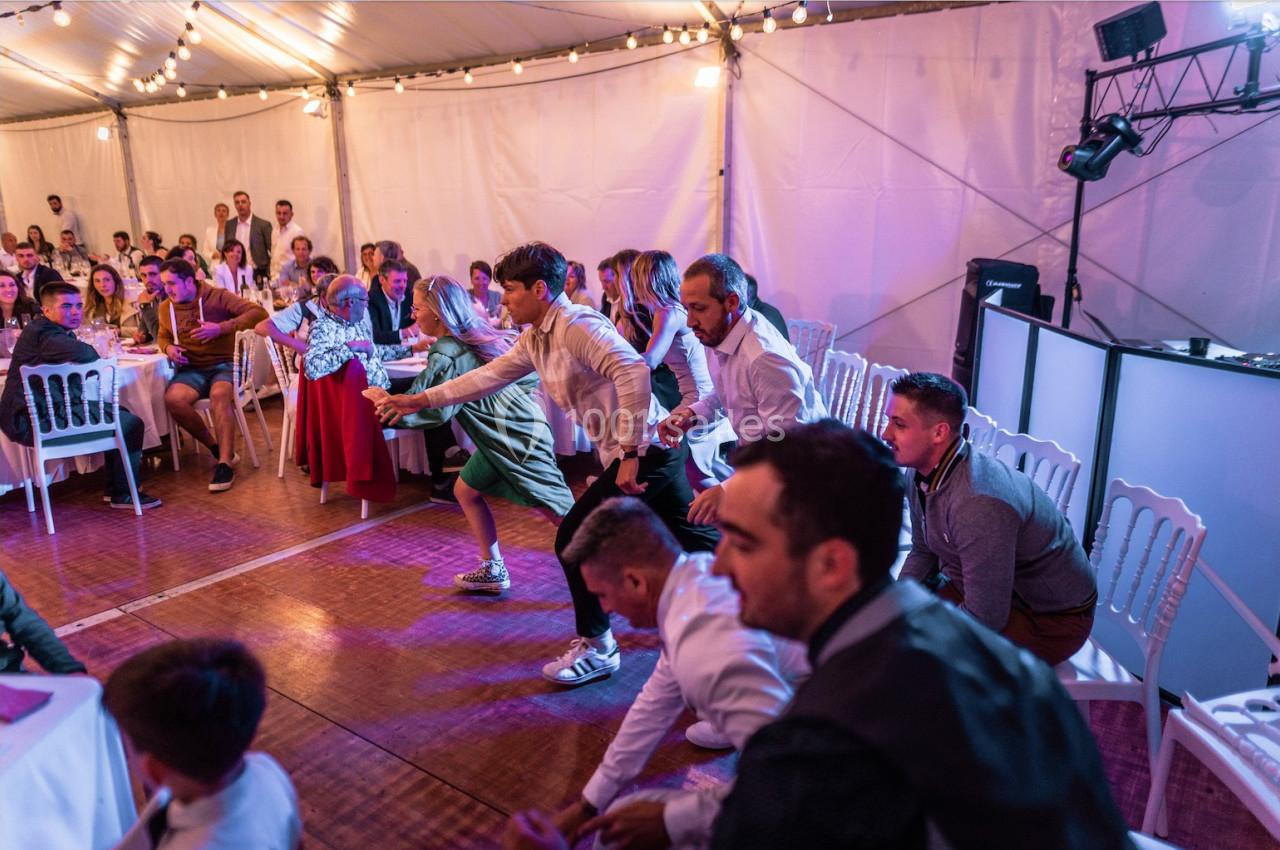 Des invités participent à une animation dansante sous un chapiteau éclairé, entourés de tables et de spectateurs.