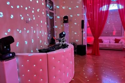 Salle de réception avec piste de danse éclairée, table de DJ équipée et décorations lumineuses rouges et blanches.