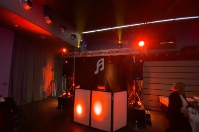 Scène de soirée avec jeux de lumières rouges et jaunes, équipement de sonorisation et table de DJ.