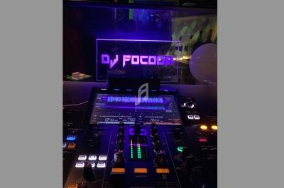 Table de mixage éclairée dans une ambiance sombre, avec un écran affichant ’DJ Focoda’ en arrière-plan.