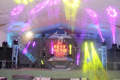 Scène de spectacle avec éclairage coloré, projecteurs et écran affichant ’The Best Music Show’.