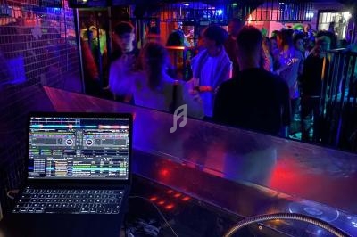 Vue d'une piste de danse animée depuis une cabine de DJ avec un ordinateur affichant un logiciel de mixage.