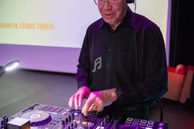 Un DJ en chemise noire mixe de la musique sur une console dans un environnement lumineux.