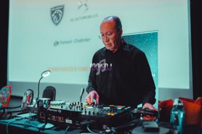 Un homme en chemise noire utilise une table de mixage lors d'un événement avec des logos projetés en arrière-plan.