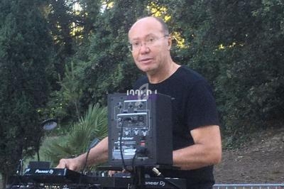Un DJ mixant en plein air devant une table de mixage, avec des arbres en arrière-plan.