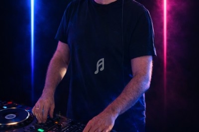 Un DJ souriant mixe de la musique sur une table de mixage, éclairé par des lumières colorées en arrière-plan.