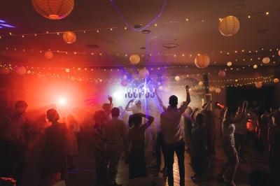 Des personnes dansent sous des lumières colorées dans une salle décorée de guirlandes lumineuses et de lanternes suspendues.