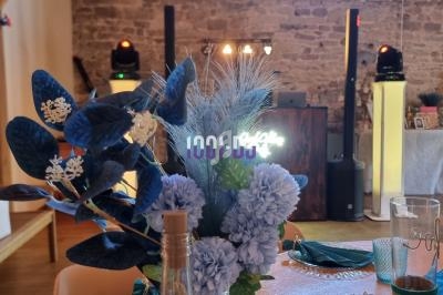 Composition florale bleue et blanche au premier plan, avec une salle décorée et un espace DJ en arrière-plan.