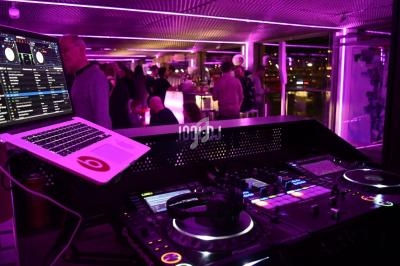 Poste de DJ avec platines et ordinateur dans un espace éclairé de lumières violettes, avec des personnes en arrière-plan.