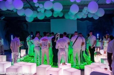 Groupe de personnes en tenue blanche réunies dans une salle décorée de ballons et éclairée par des lumières colorées.