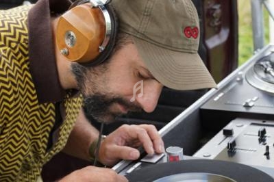 Un homme portant un casque audio ajuste un disque vinyle sur une platine lors d'une session musicale en extérieur.