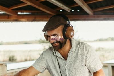 Un homme souriant mixe des disques vinyles sur une platine sous un abri en bois.