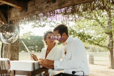 Un couple examine des vinyles sous une pergola en bois, avec une boule disco suspendue et un paysage verdoyant en arrière…