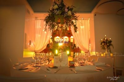 Table élégamment dressée avec des verres, des bougies et un centre de table floral, dans une salle éclairée chaleureusement.