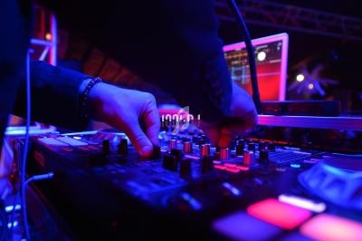 Mains ajustant les commandes d'une console de mixage audio dans un environnement lumineux et technologique.