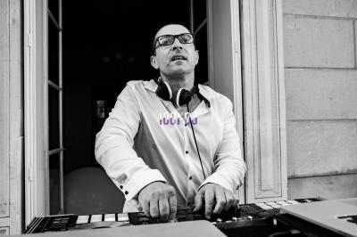 Homme portant un casque audio, debout devant une table de mixage, dans l'encadrement d'une porte ouverte.