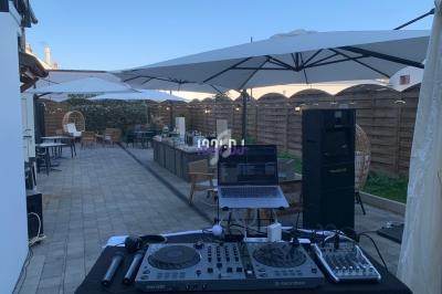 Table de mixage avec ordinateur et enceintes installés en extérieur sous des parasols dans une cour pavée.