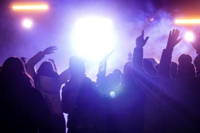 Groupe de personnes levant les bras devant des lumières vives dans une ambiance de concert ou d'événement nocturne.
