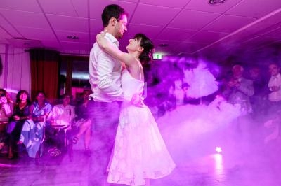 Un couple danse dans une salle éclairée par des lumières violettes, entouré de spectateurs assis et debout.