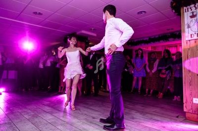 Un couple danse sur une piste éclairée de lumières roses, entouré de spectateurs dans une salle festive.