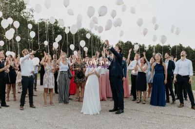 Un groupe de personnes, en tenue de cérémonie, lâche des ballons blancs dans un espace extérieur.
