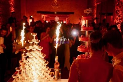 Un couple observe une fontaine de champagne et un gâteau illuminés par des cierges, entourés d'invités dans une salle…