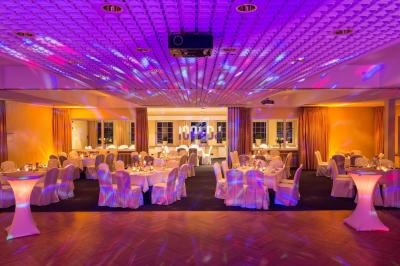 Salle de réception décorée avec des tables rondes dressées, éclairage coloré et ambiance festive.