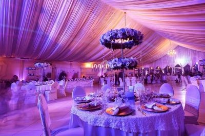 Salle de réception décorée avec des tables rondes élégantes, nappes blanches et éclairage tamisé violet.