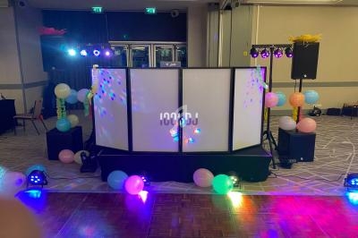 Stand de DJ éclairé avec des jeux de lumière colorés, entouré de ballons dans une salle de réception.