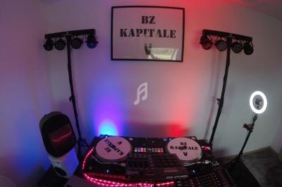 Poste de DJ avec platines, table de mixage, éclairages colorés et panneau ’BZ KAPITALE’ sur le mur.