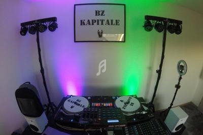 Équipement de DJ avec platines, table de mixage et éclairages colorés dans une pièce décorée sobrement.
