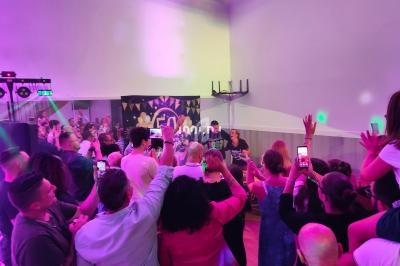 Groupe de personnes dans une salle éclairée par des lumières colorées, certaines prenant des photos ou applaudissant.