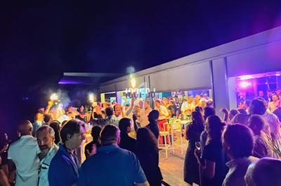 Groupe de personnes rassemblées en soirée festive en extérieur, éclairée par des lumières colorées.