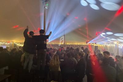 Groupe de personnes dans une ambiance festive sous une tente éclairée par des lumières colorées.