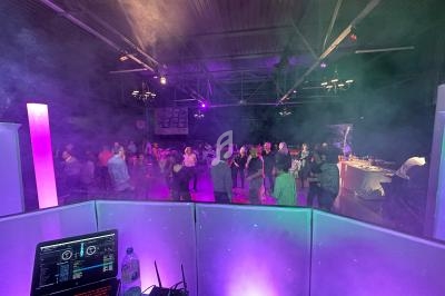 Vue depuis une cabine de DJ sur une piste de danse animée, éclairée par des lumières colorées et entourée de fumée légère.