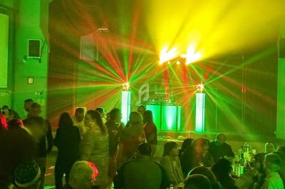 Des personnes dansent dans une salle éclairée par des jeux de lumière colorés provenant d'une scène avec un DJ.