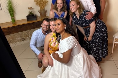 Un groupe de personnes posant ensemble dans une pièce lumineuse, avec une femme en robe blanche au premier plan.