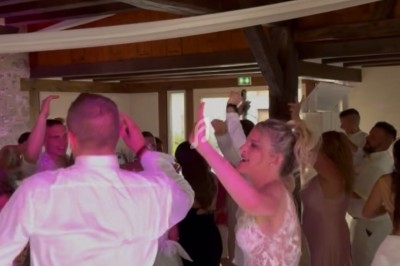 Des invités dansent joyeusement lors d'une réception de mariage dans une salle en bois avec éclairage coloré.
