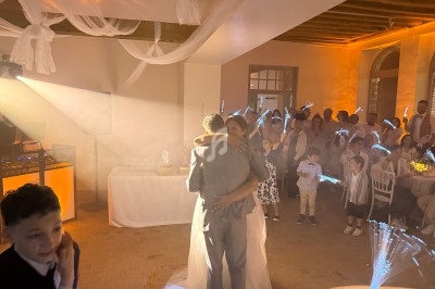 Un couple danse enlacé au centre d'une salle éclairée, entouré d'invités tenant des bâtons lumineux.