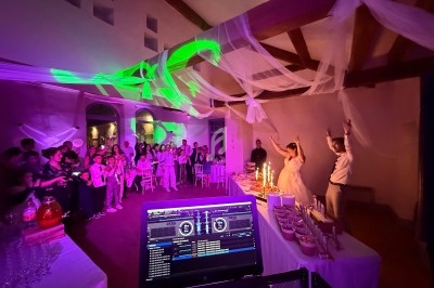 Salle de réception décorée, ambiance festive avec des invités, un couple célébrant et une table de buffet éclairée.