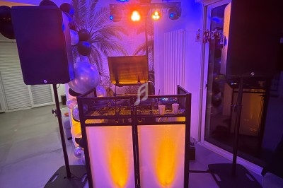 Installation de matériel de DJ avec lumières colorées, enceintes et table de mixage dans une pièce décorée.